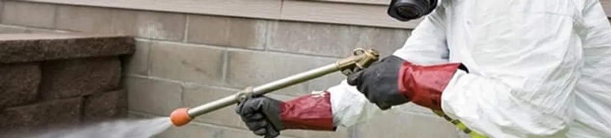 Pest control technician applying exterior insect treatment along a home foundation in Boulder, CO