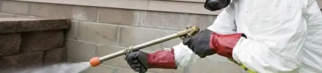 Pest control technician applying exterior insect treatment along a home foundation in Boulder, CO
