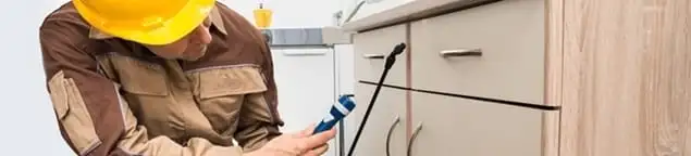 Roach exterminator applying treatment under kitchen cabinets in Boulder, CO