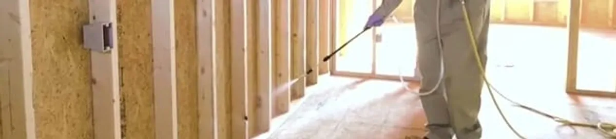 Termite treatment technician applying spray along framing and unfinished walls in Boulder, CO